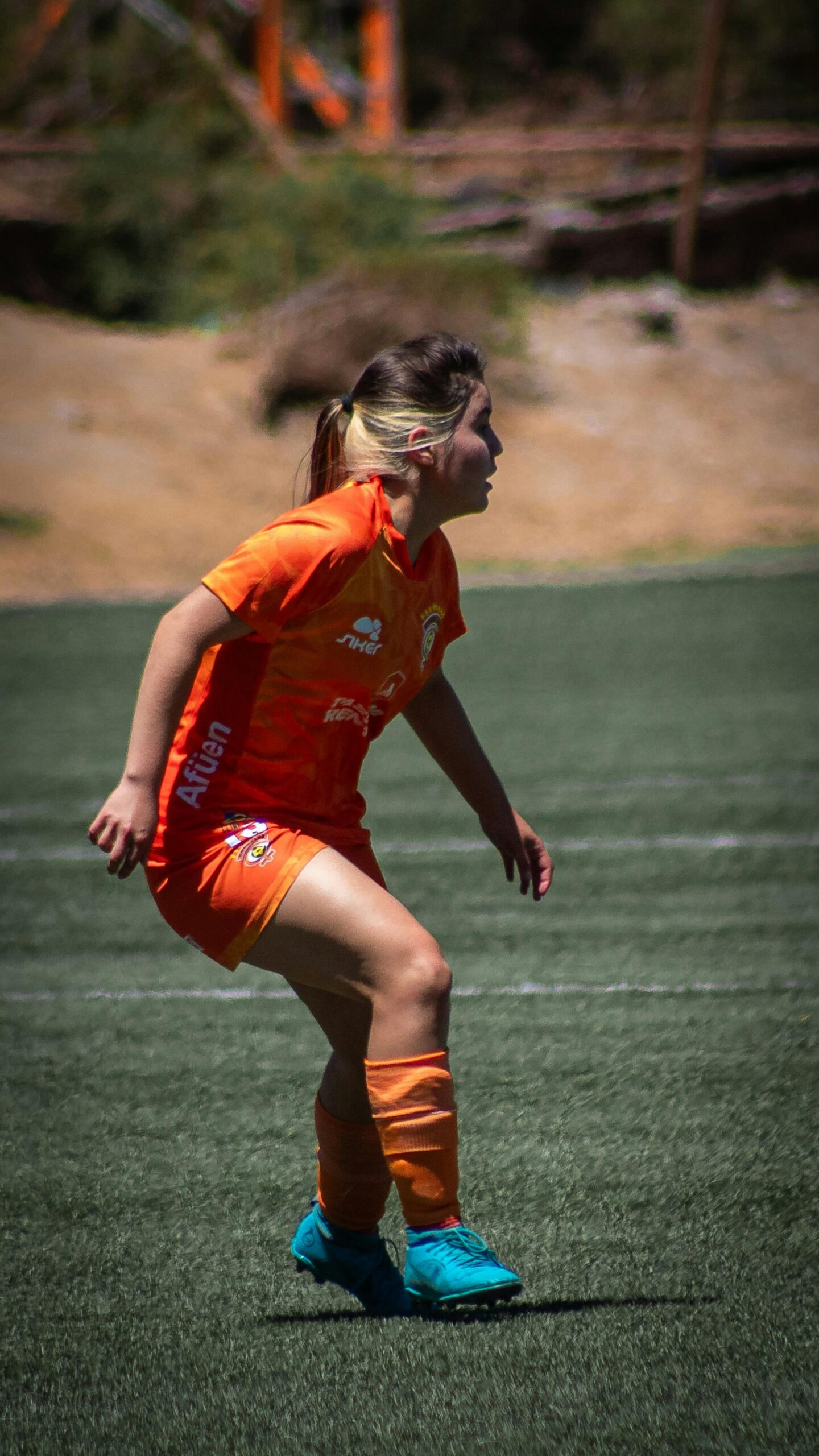 Female soccer player in bright orange uniform in action on a sunny day.